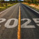 An open road stretching into the horizon with the year '2025' painted on the asphalt, symbolizing a journey toward the future. Surrounded by greenery and mountains in the distance under a warm sunset glow.